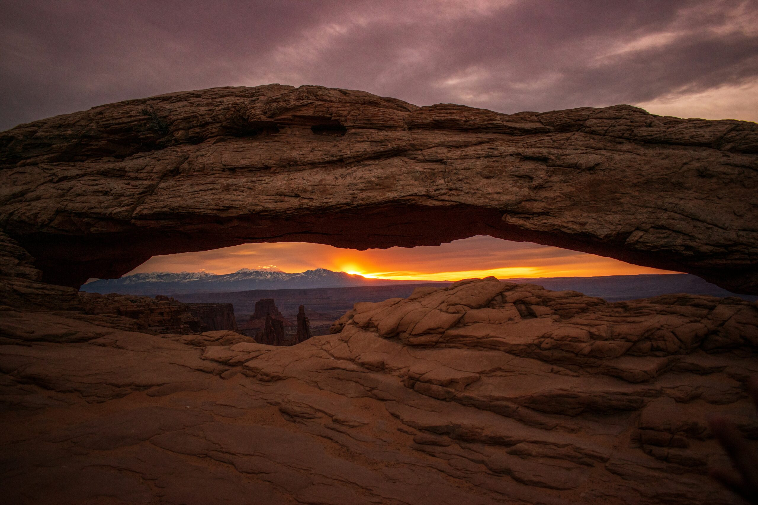 Mesa Arch at sunrise in Canyonlands National Park glowing orange as light filters through the sandstone span over the canyon below