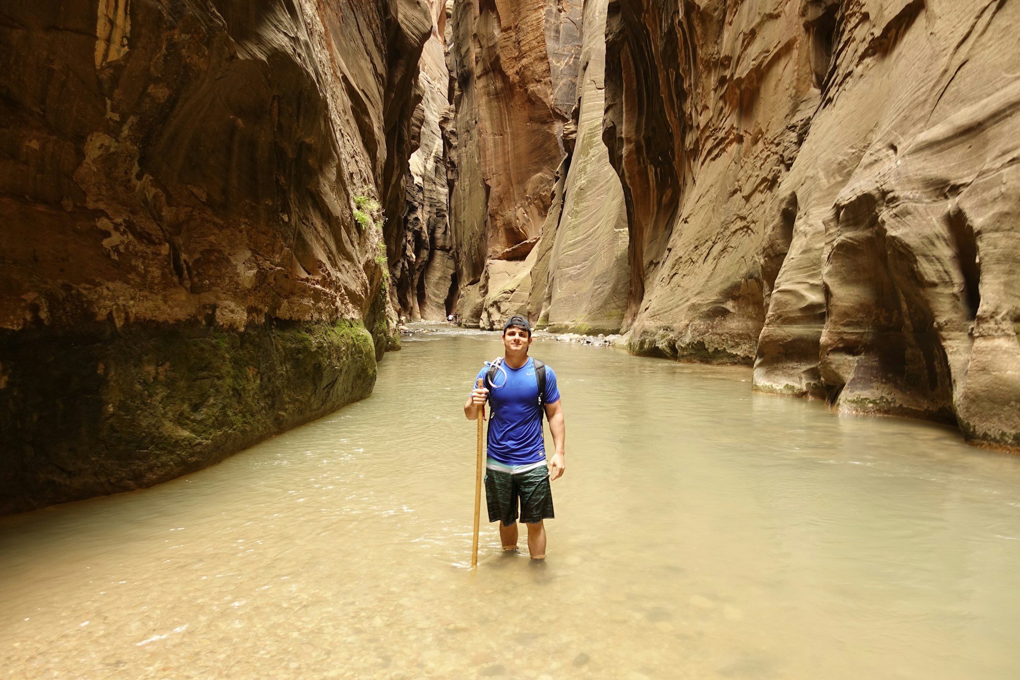 Hikers wading the Virgin River through the towering slot walls of The Narrows in Zion National Park